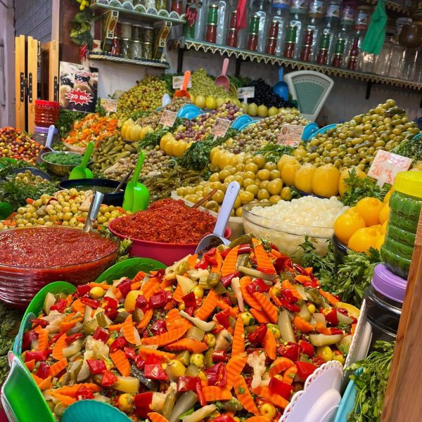 A stall in the Souk of the Marrakech medina selling an array of beautiful local produce, mixed vegetables, all varieties and colours of olives, preserved lemons, with jars of spices in the background. Natural Morocco