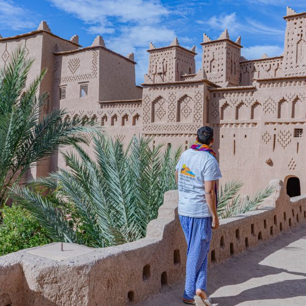 Tour guide looking at the famous view of Kasbah Ameridil in Skoura, this view once appeared on the 50 Dirham note in Morocco. The view shows the mud brick walls of the Kasbah, the contrasting blue sky and the tops of the palm trees in the courtyard below. Morocco Uncovered