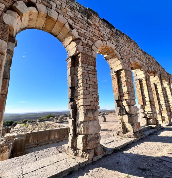 View of a row of arches at the ancient Roman ruins of Volubilis, with blue sky in the background Moroccan Mystery